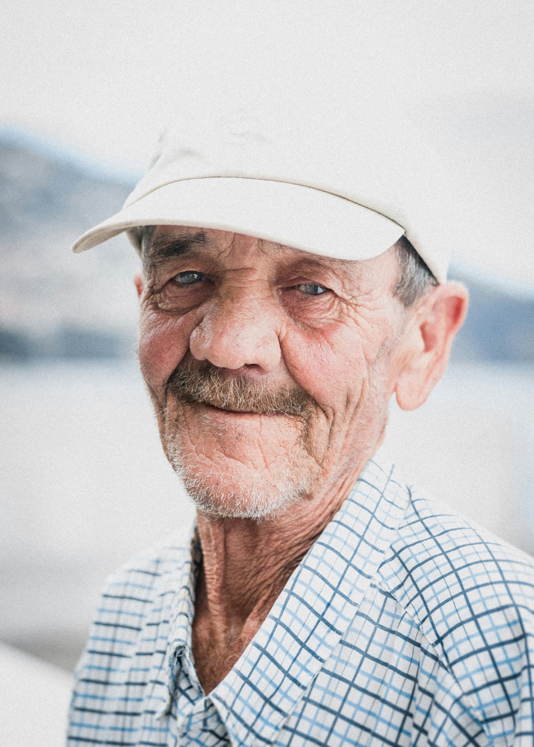 An older man smiling in a white cap